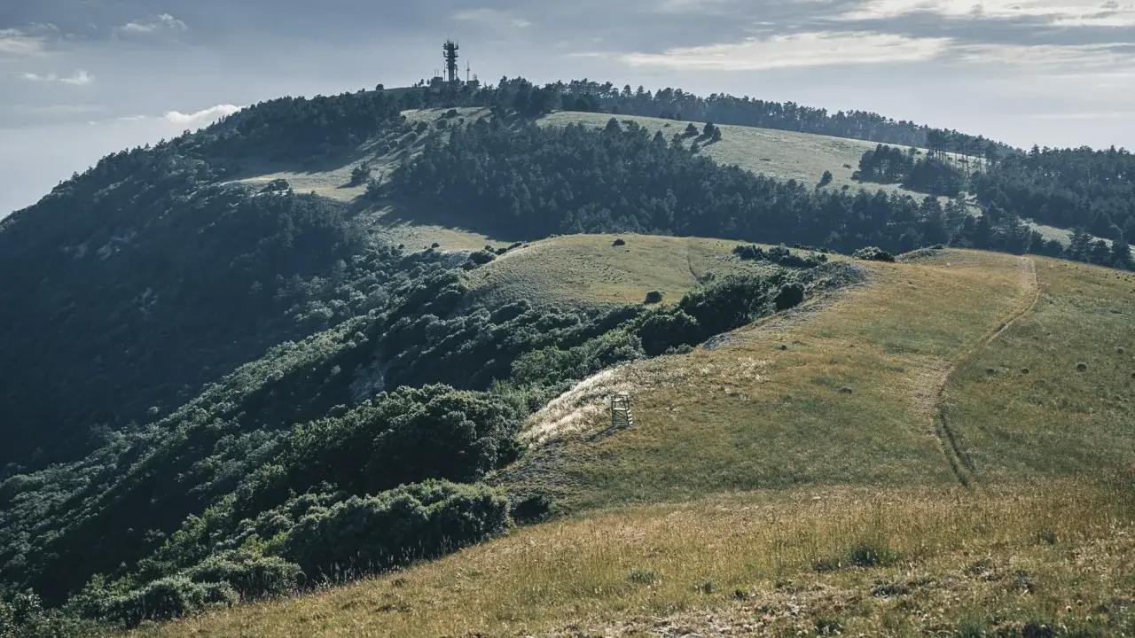 Vue panoramique du Moure Negre, avec une tour de télécommunication au sommet, des collines verdoyantes et un sentier sinueux.