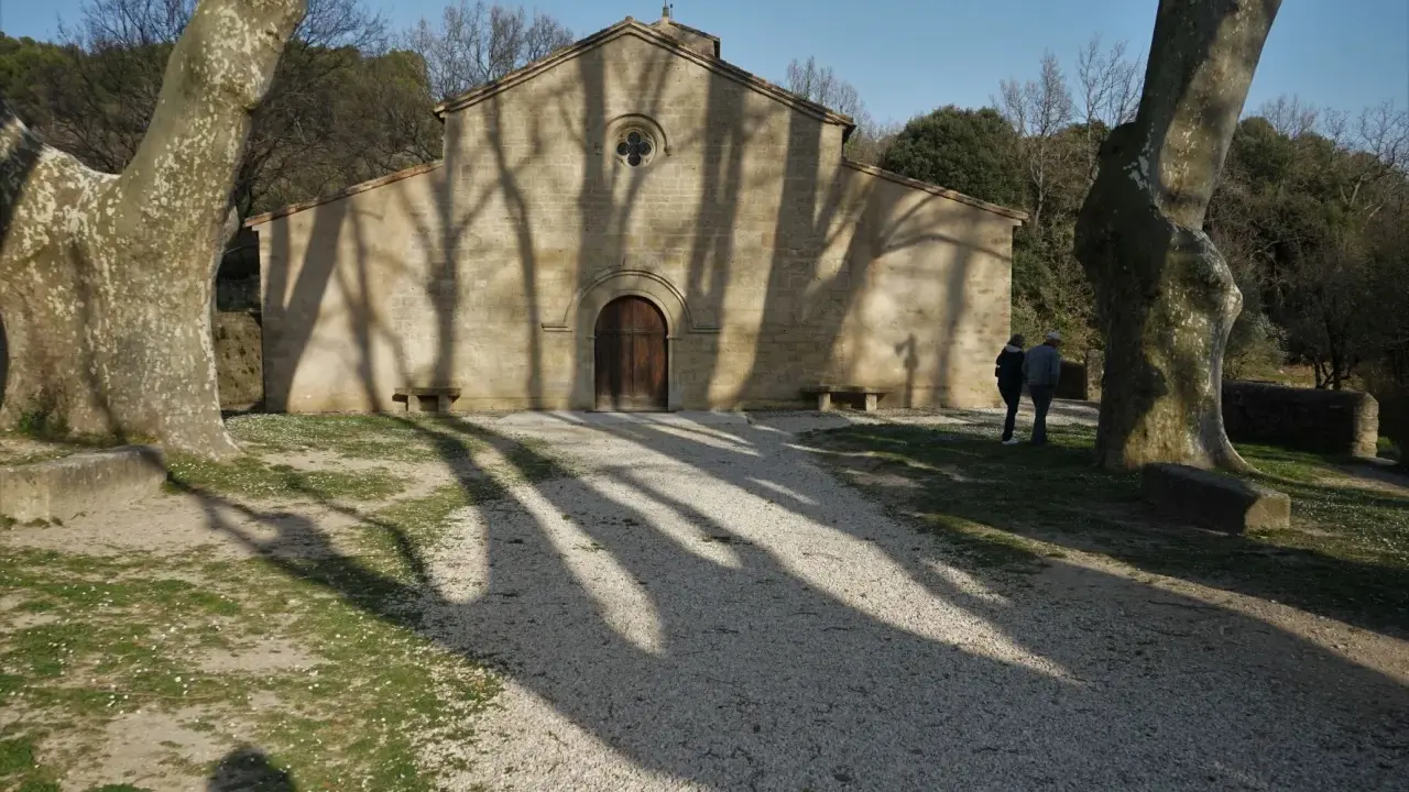 L'église de Vaugines, baignée de soleil, accueille deux visiteurs. Les ombres des arbres dansent sur sa façade de pierre.