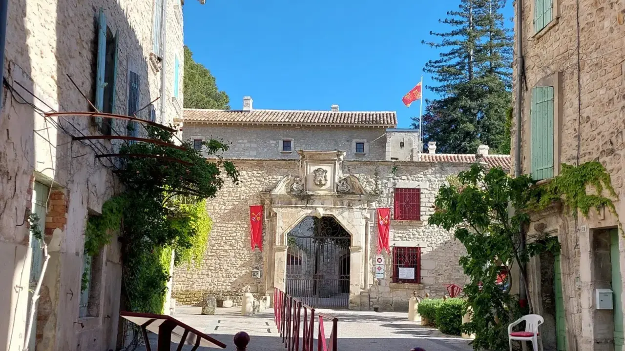 L'entrée majestueuse du **château de Thézan** s'ouvre sur une cour pavée, ornée de drapeaux rouges et d'une végétation luxuriante.