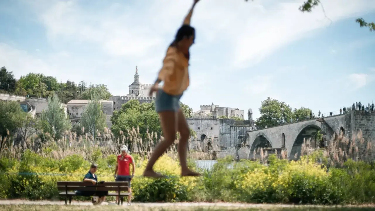 Amusez-vous à Avignon ce week-end ! Une jeune femme saute devant le Palais des Papes et le Pont d'Avignon.