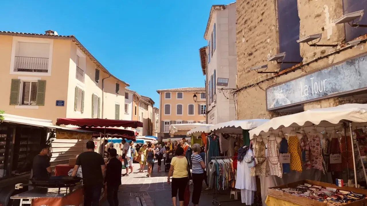 Animation des étals colorés et des passants sous le soleil éclatant du marché de l'Isle-sur-la-Sorgue.