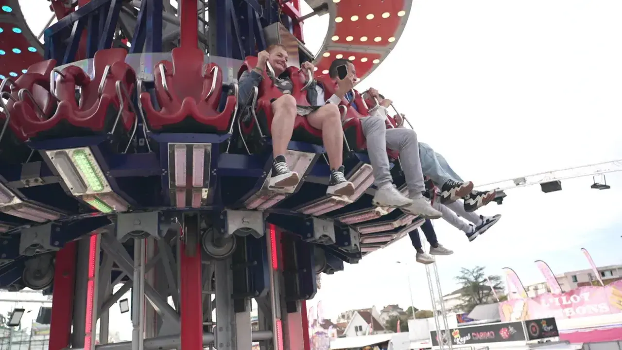Des jeunes s'amusent dans une attraction de la fete foraine 84, leurs pieds balançant dans le vide.