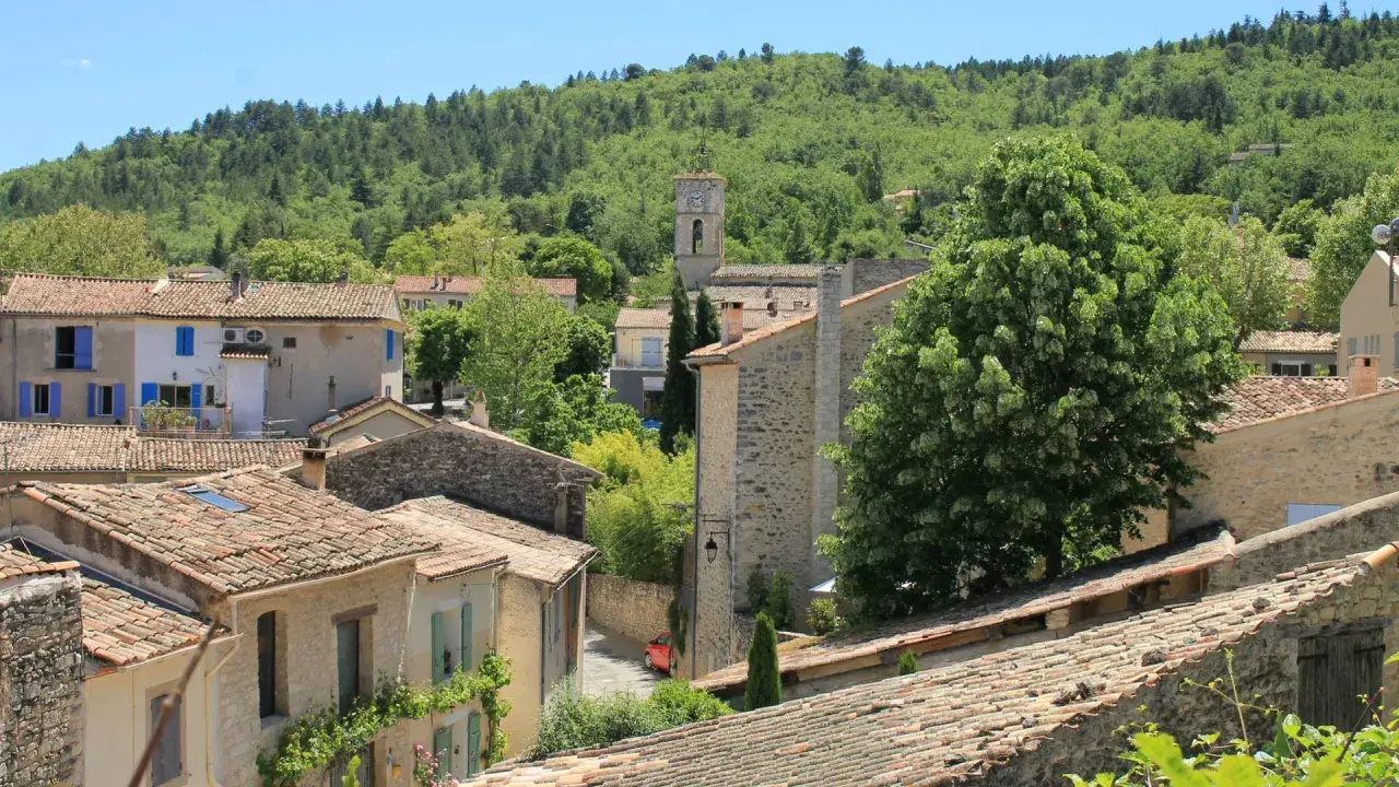 Vue d'un village provençal avec ses toits de tuiles, un clocher et une colline boisée. On imagine le marché de Cereste animé sous le soleil.