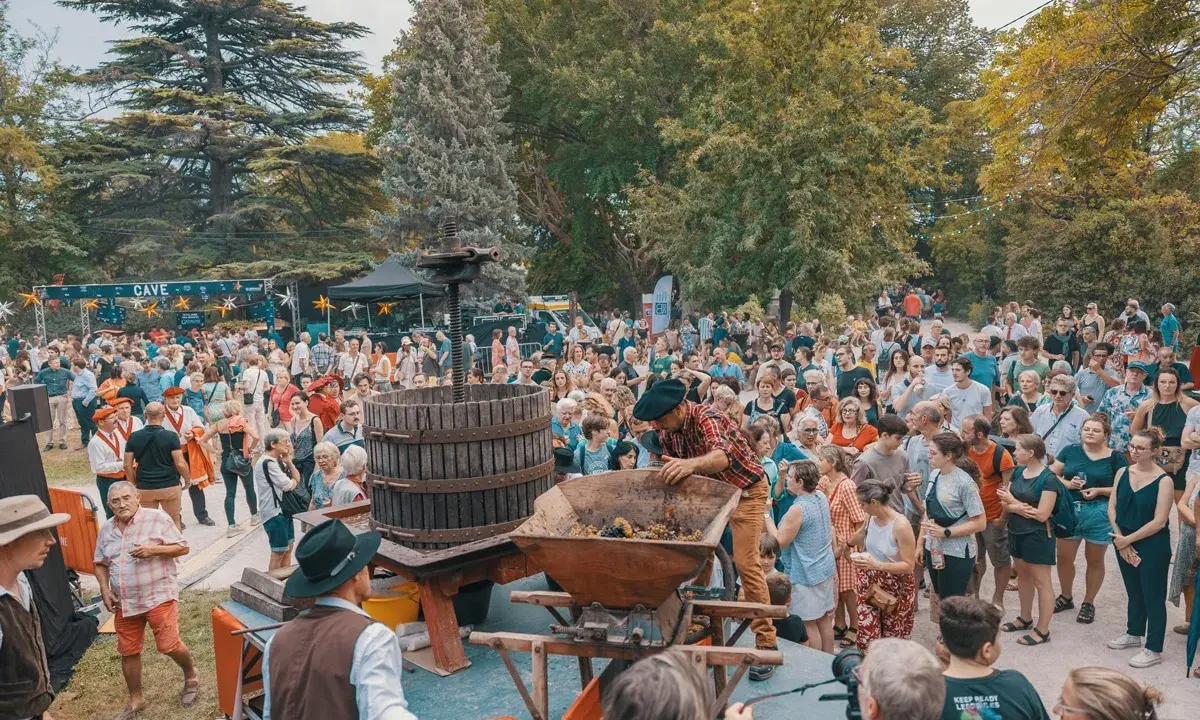 Foule joyeuse à Avignon pour le ban des vendanges, avec un pressoir à vin traditionnel au centre.