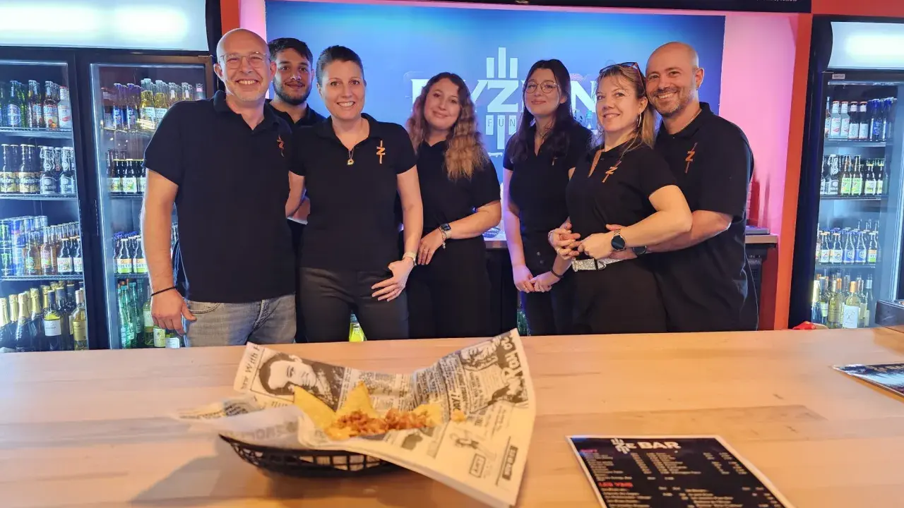 L'équipe du bar Elyzion, souriante, pose devant les réfrigérateurs. Sur le comptoir, des nachos et un menu.