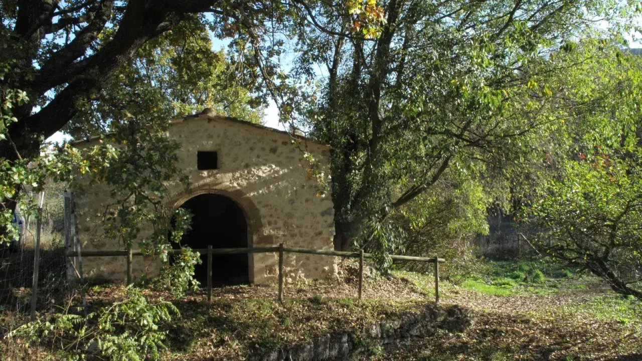 Ancienne bâtisse en pierre avec une arche, entourée d'arbres feuillus et d'une clôture en bois. Un lieu paisible dans le parc de l'arbousière.