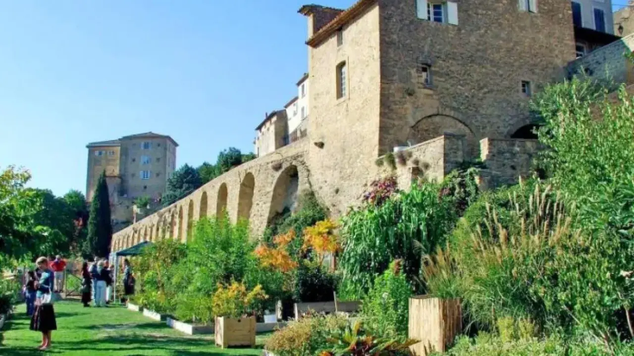 Jardin luxuriant devant le **château de Lauris**, avec ses murs de pierre et ses arches médiévales.