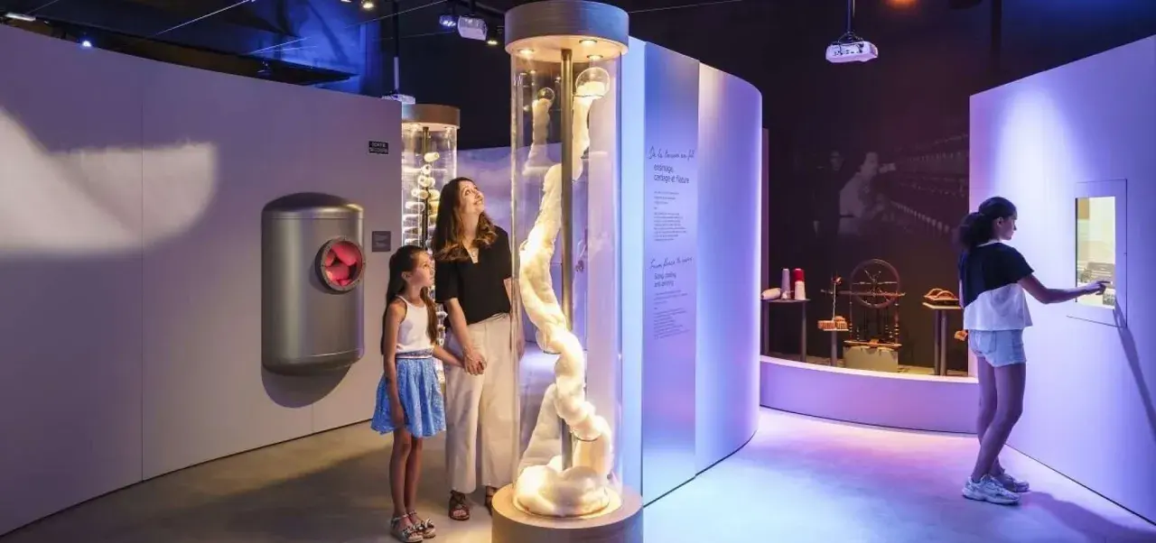 Une mère et sa fille découvrent la filaventure dans un musée interactif, fascinées par une colonne de fibres.
