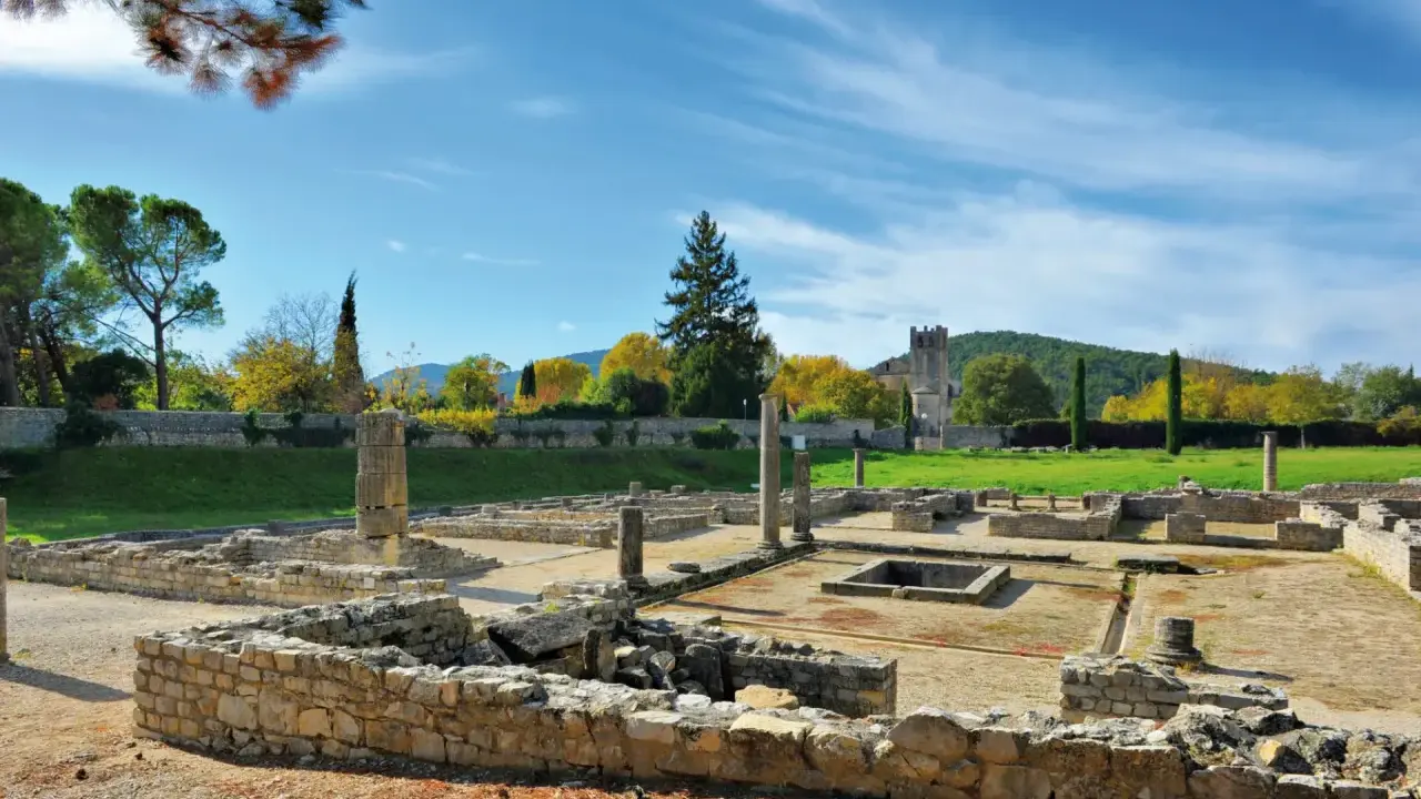 Vestiges romains ensoleillés, parfaits pour visiter Vaison-la-Romaine. Ruines antiques, colonnes et un clocher médiéval en arrière-plan.