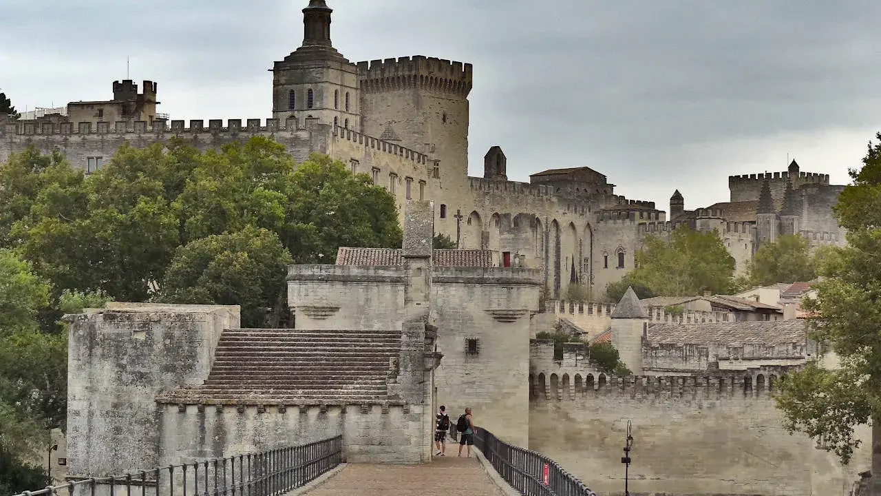 Le Palais des Papes, un incontournable pour tout guide Avignon, se dresse majestueusement. Des touristes explorent ce site historique.