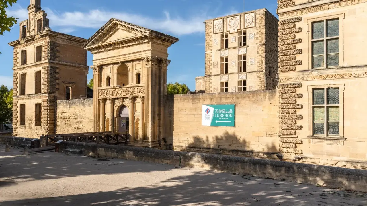 La Tour d'Aigues, un château Renaissance en Provence, se dresse sous un ciel bleu. Une passerelle en bois mène à son entrée ornée.