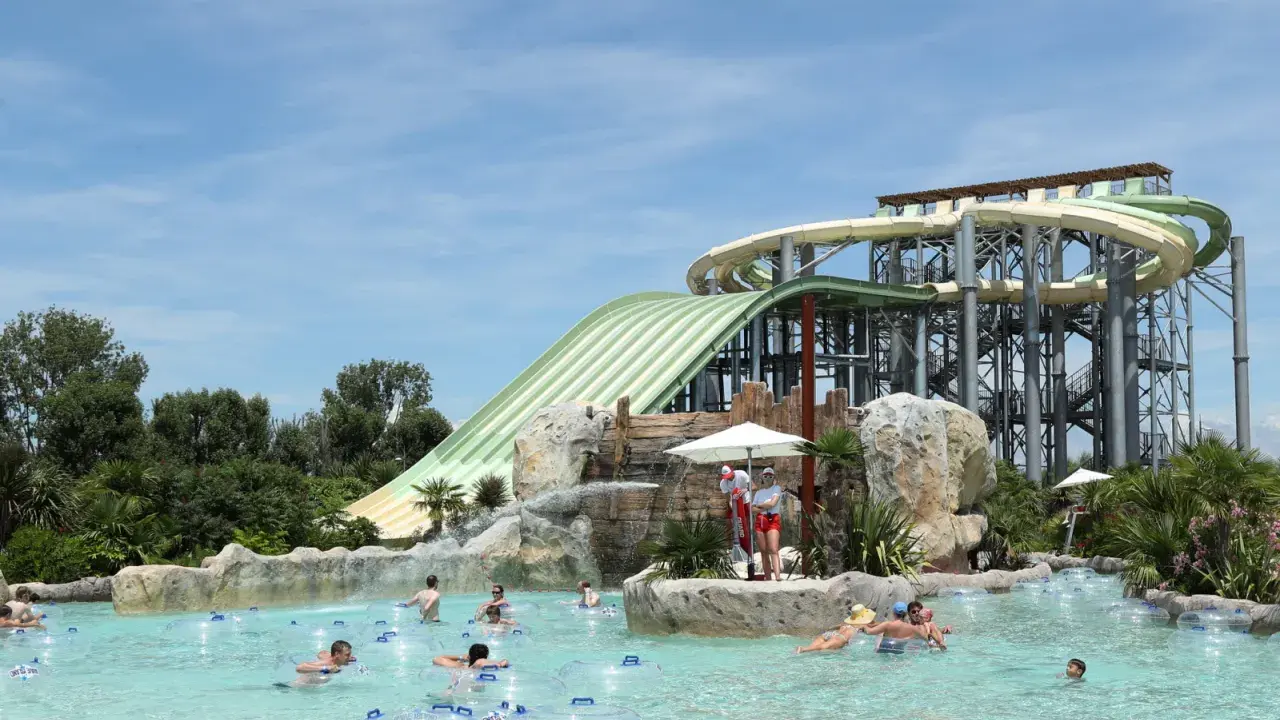 Ambiance estivale dans un parc aquatique Vaucluse. Des familles profitent de la piscine à bouées, sous les imposants toboggans verts et blancs.