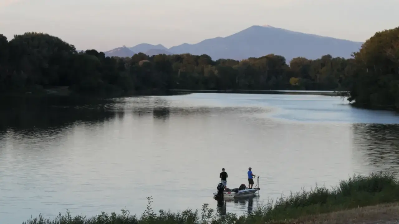 Deux pêcheurs sur un bateau profitent du calme du plan d'eau du Revestidou, avec des montagnes en arrière-plan.