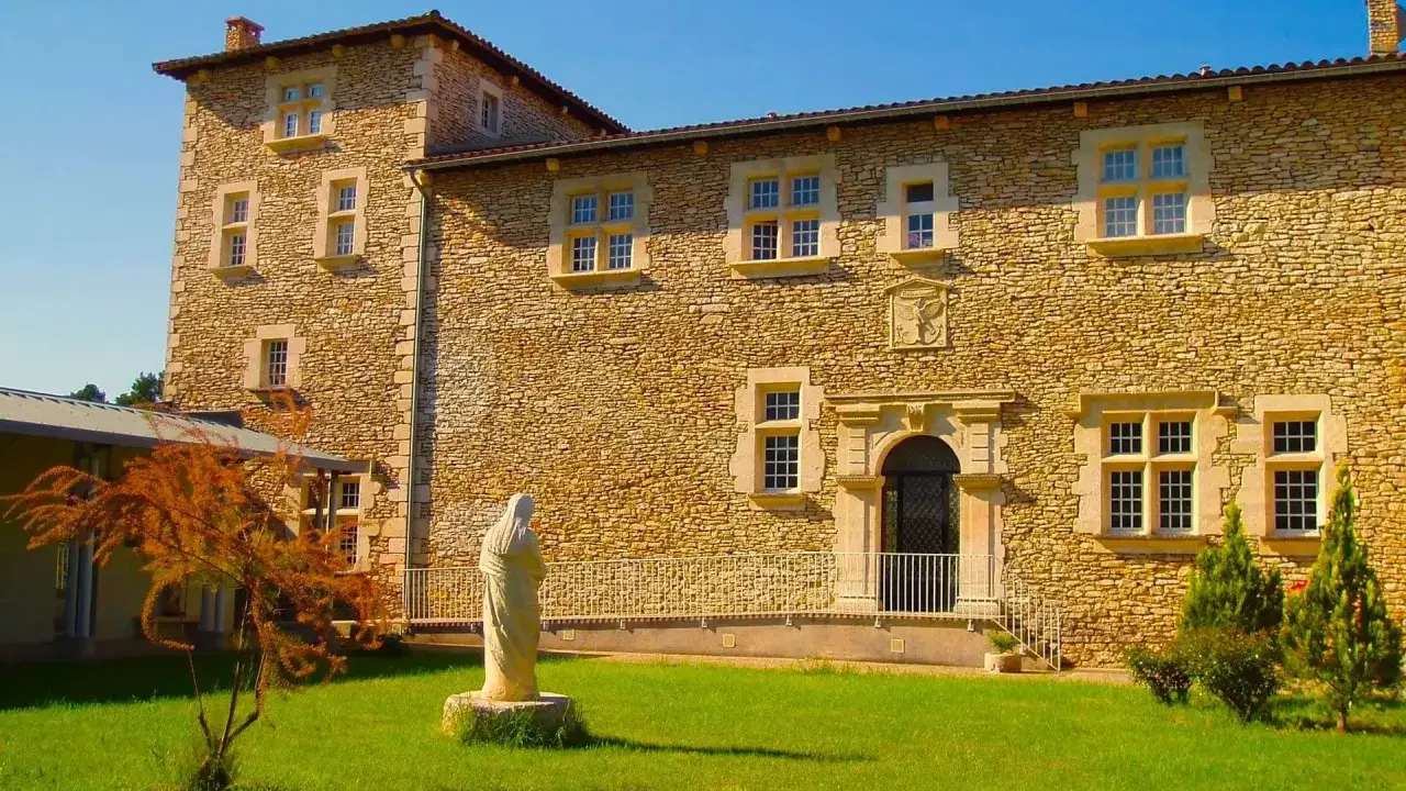Statue de la Vierge devant la façade en pierre de la blauvac abbaye, sous un ciel bleu éclatant.