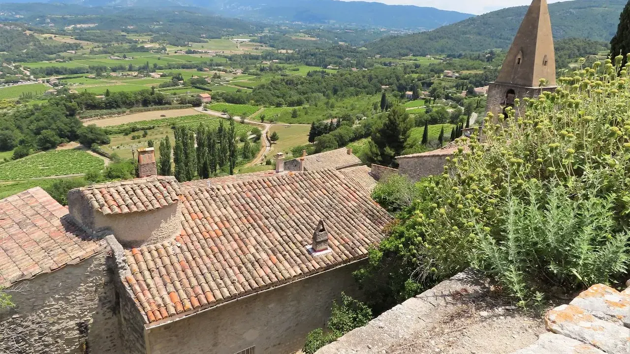 Vue panoramique d'un village provençal avec ses toits de tuiles, sa campagne verdoyante et ses montagnes. Une belle activité gratuite Vaucluse pour s'évader.