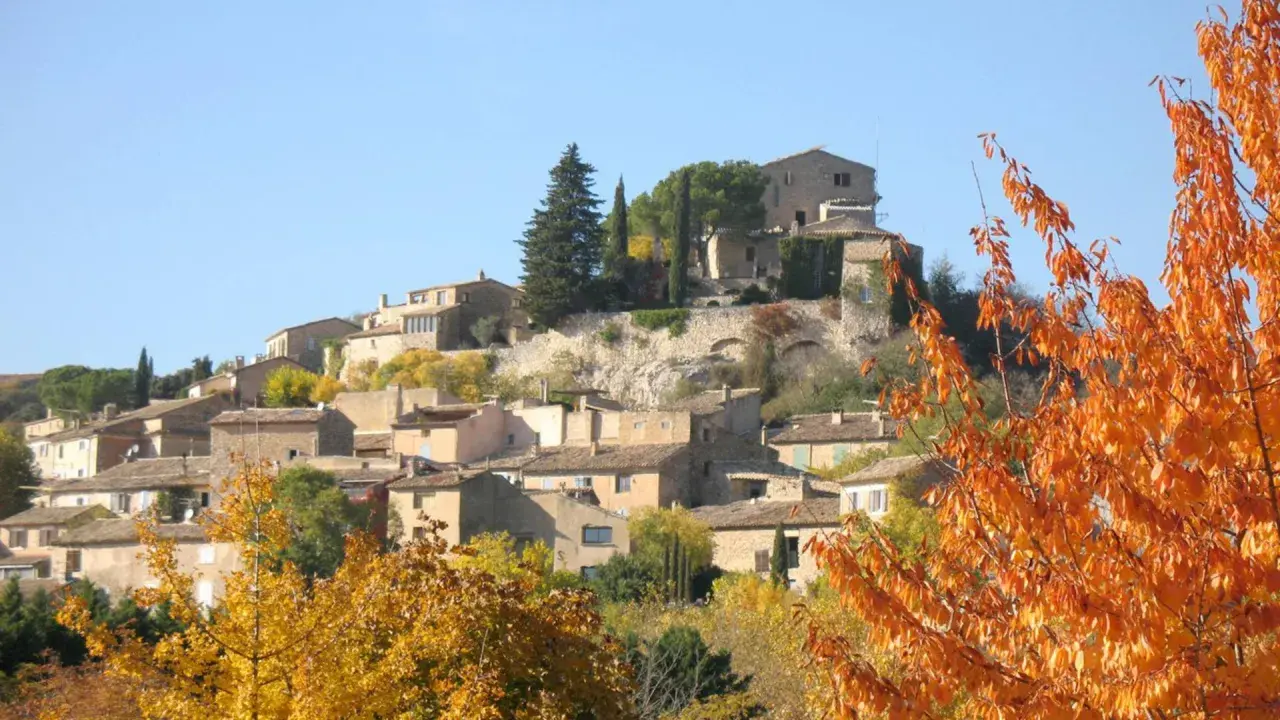 Village de Joucas, France, en automne. Les maisons en pierre s'étagent sur la colline, entourées d'arbres aux couleurs flamboyantes.