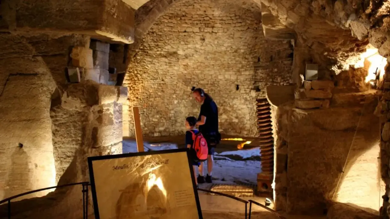 Un homme et un enfant explorent les caves du palais saint-firmin, un lieu historique aux voûtes de pierre.