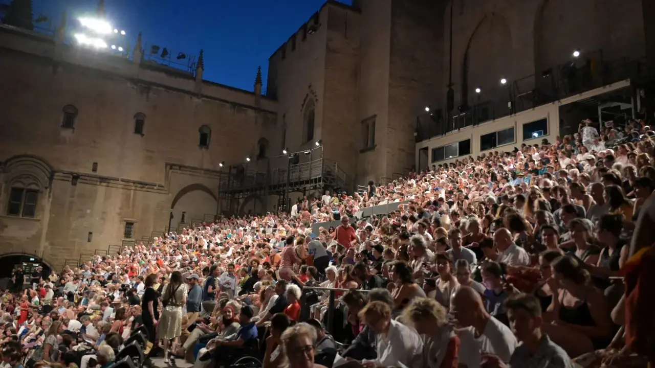 Foule nombreuse assise sur des gradins, devant un palais, pour la Fête de la Musique à Avignon.