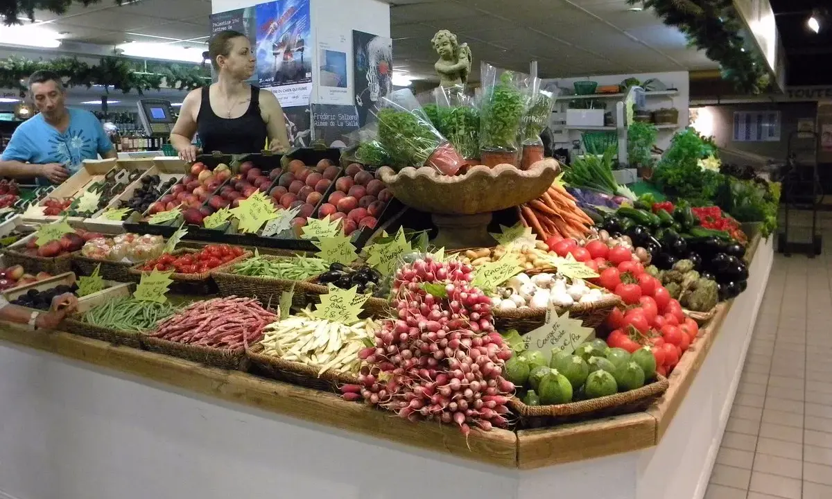 Un étal coloré au marché d'Avignon présente une abondance de fruits et légumes frais : pêches, tomates, haricots verts, radis, aubergines, et plus encore.