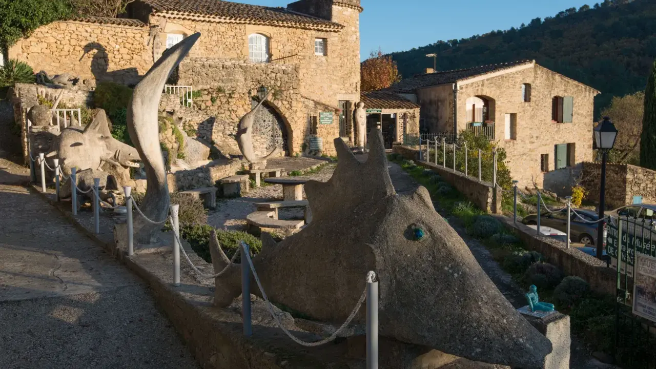 Sculptures étranges devant le musée extraordinaire Ansouis. Un chemin serpente entre des créatures de pierre et des bâtiments en pierre.