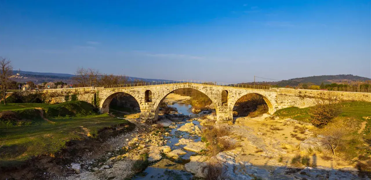 Le **pont Julien**, un ancien pont de pierre à trois arches, enjambe une rivière asséchée bordée de rochers et de végétation.