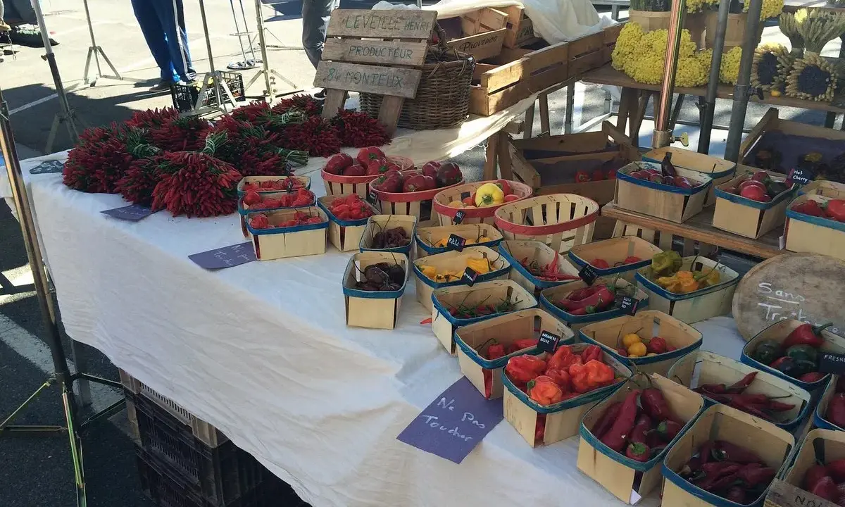 Au marché de Carpentras, des piments rouges vifs et des poivrons colorés sont présentés dans des paniers en bois.