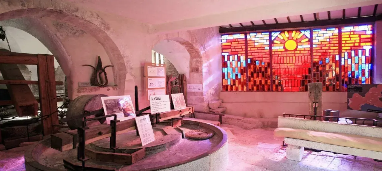 Dans le musée du vitrail Gordes, une roue de moulin ancienne côtoie un vitrail éclatant de soleil et de couleurs chaudes.