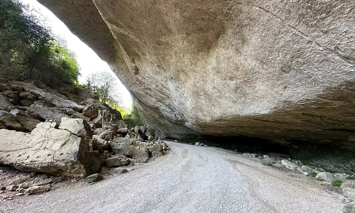 Le chemin menant au fort de Buoux serpente sous un immense surplomb rocheux, offrant un aperçu de la nature sauvage.