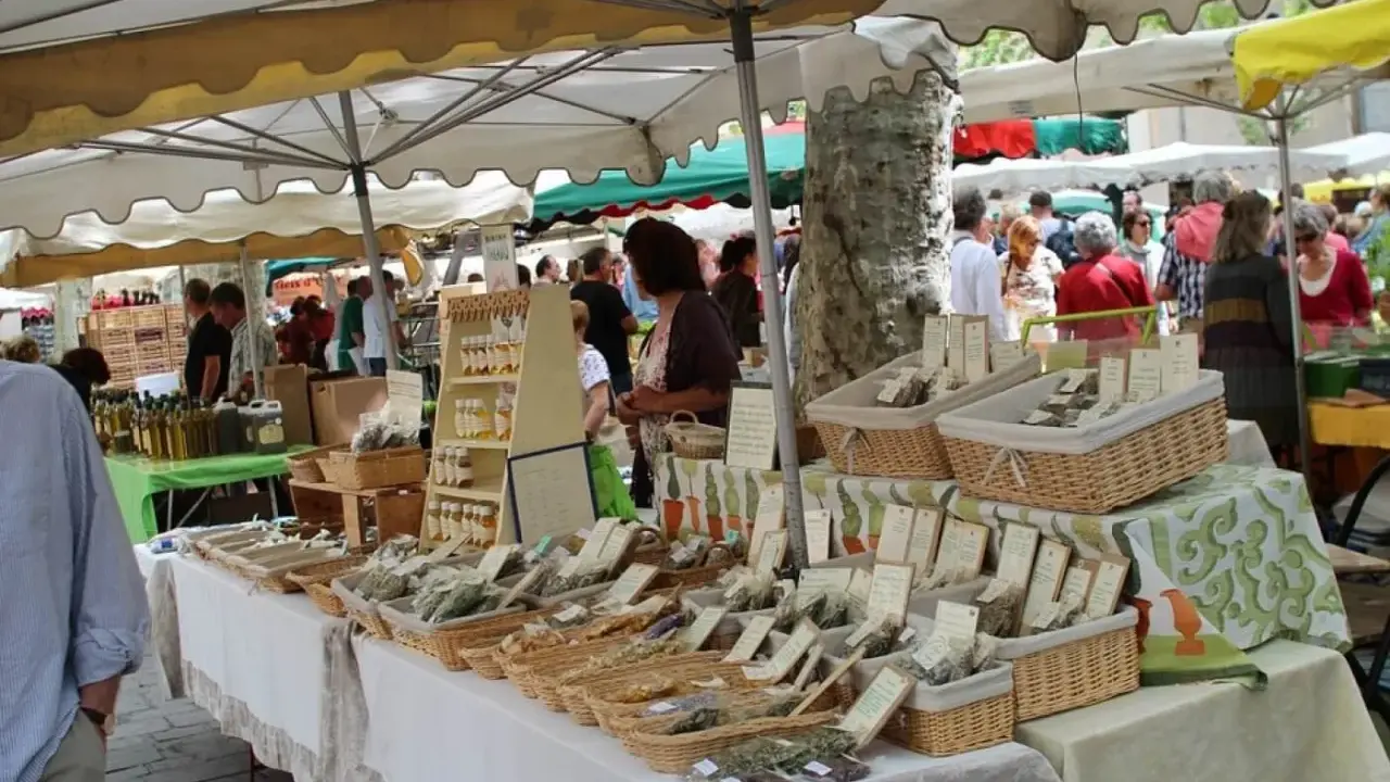 Ambiance animée au marché de Lourmarin, avec des étals de produits locaux, herbes aromatiques et bouteilles d'huile d'olive.