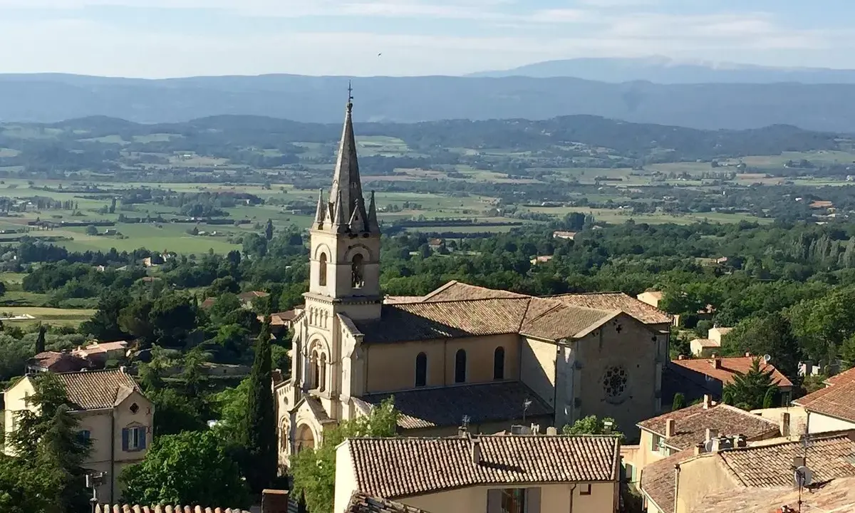 Vue panoramique sur Bonnieux, France, avec son église et ses toits de tuiles, dominant une vallée verdoyante.