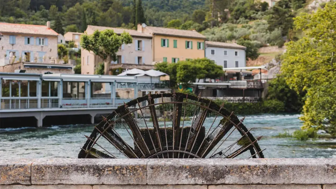 Roue à aubes rouillée sur la Sorgue, avec des maisons provençales en arrière-plan. Le **gouffre de Fontaine-de-Vaucluse** est une source d'eau d'une beauté saisissante.