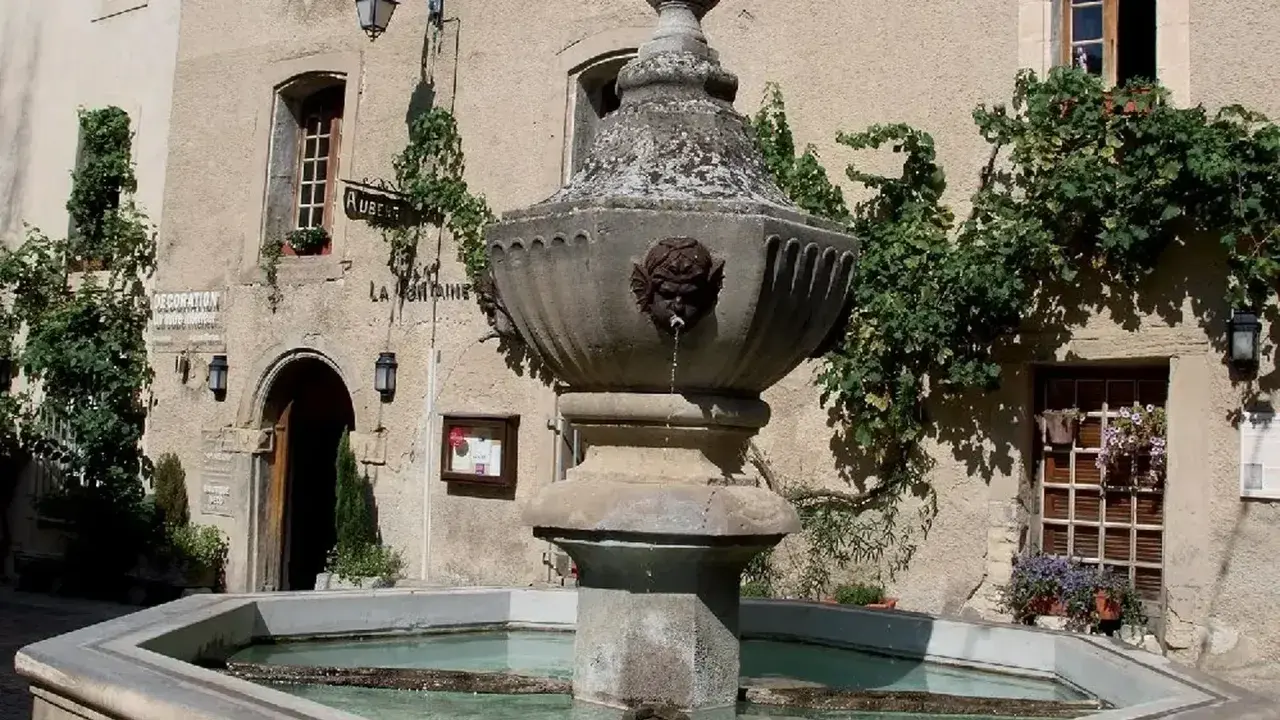 Fontaine en pierre avec des têtes de gargouilles à Venasque, Vaucluse. L'eau coule doucement dans le bassin, entouré de végétation luxuriante.