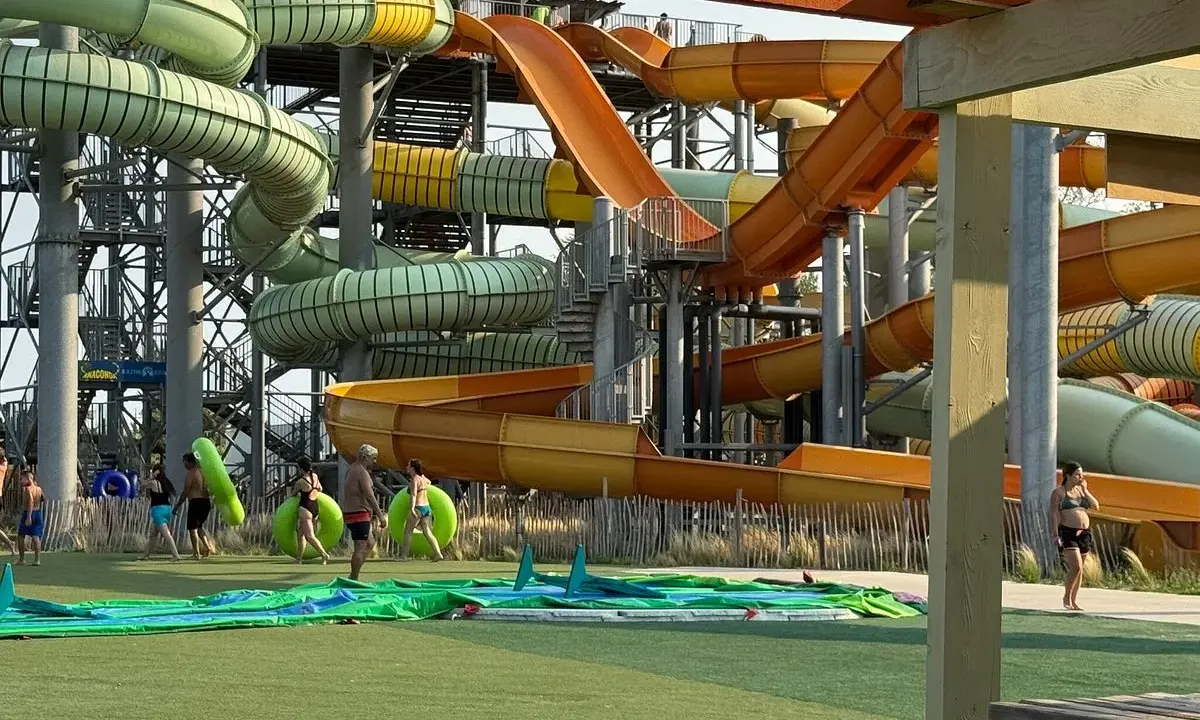 Des toboggans colorés et sinueux dominent le parc aquatique de Monteux. Des visiteurs se préparent à glisser, certains portant des bouées vertes.