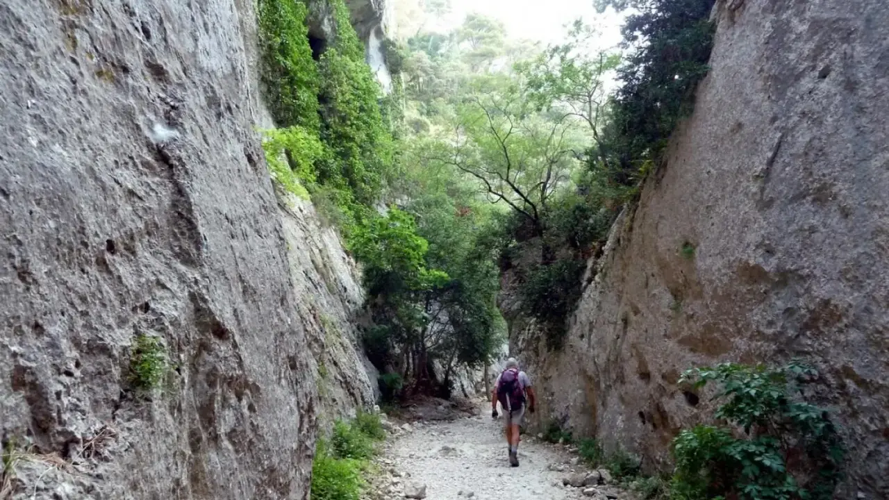 Un randonneur explore les **gorges du Régalon**, un sentier rocailleux bordé de falaises abruptes et de végétation luxuriante.