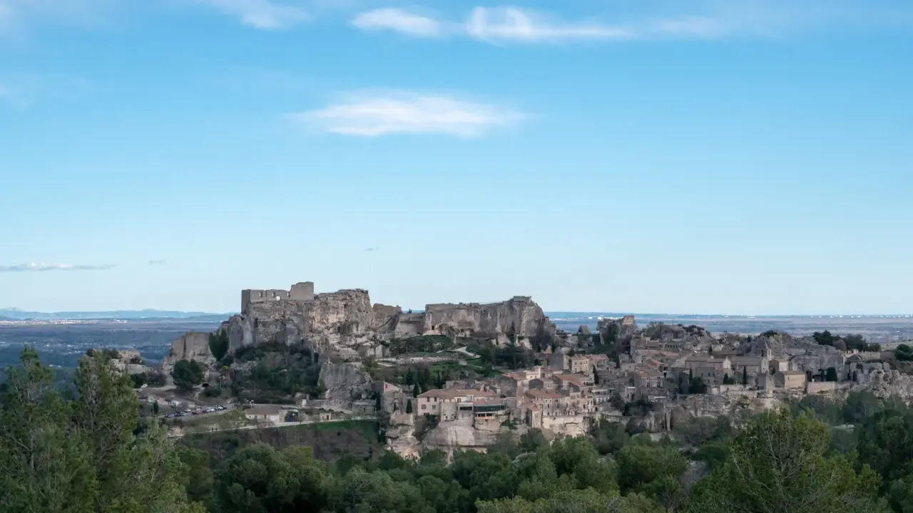 Vue panoramique du village perché des Baux-de-Provence, avec son château médiéval en ruines dominant les maisons de pierre et la végétation verdoyante.