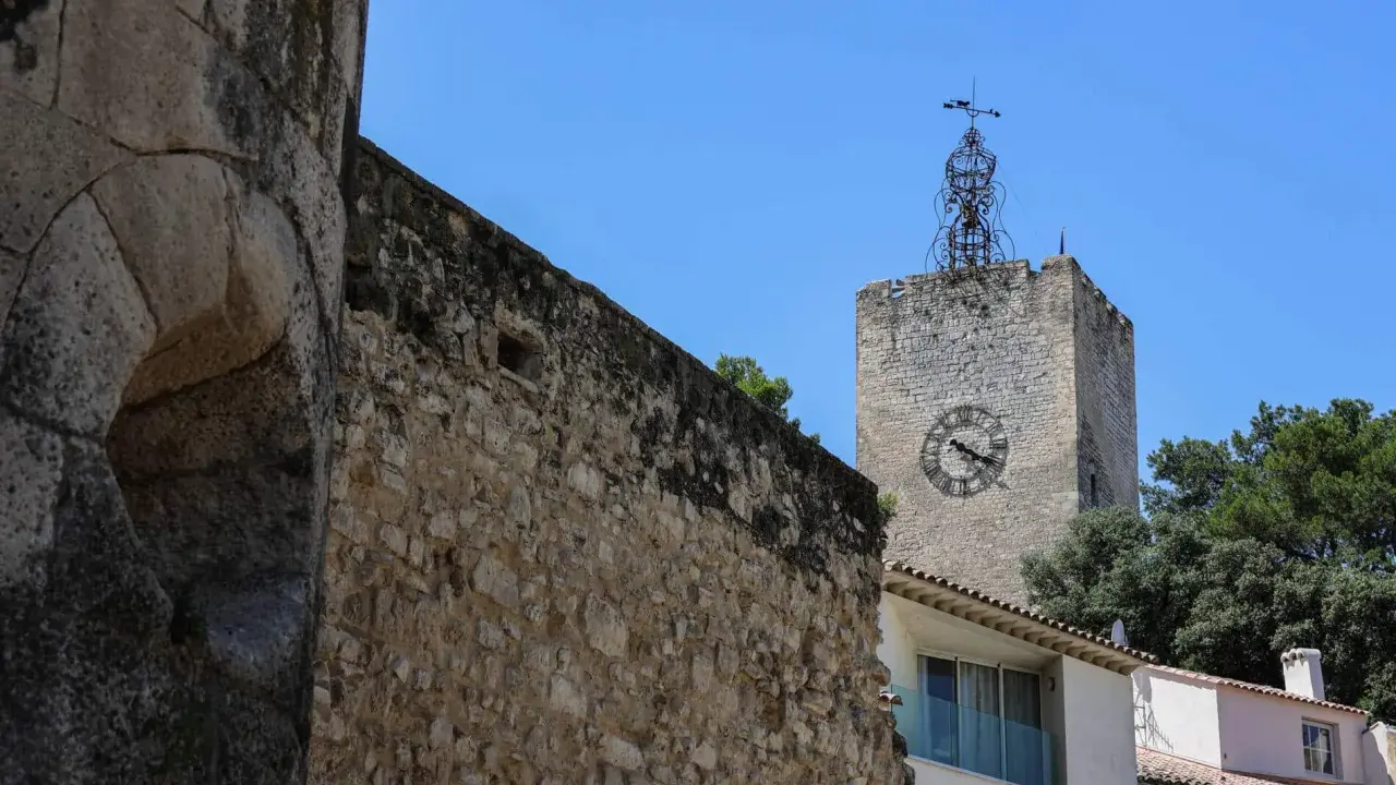 Vieille tour de l'horloge à Pernes-les-Fontaines, avec un mur de pierre ancien au premier plan.