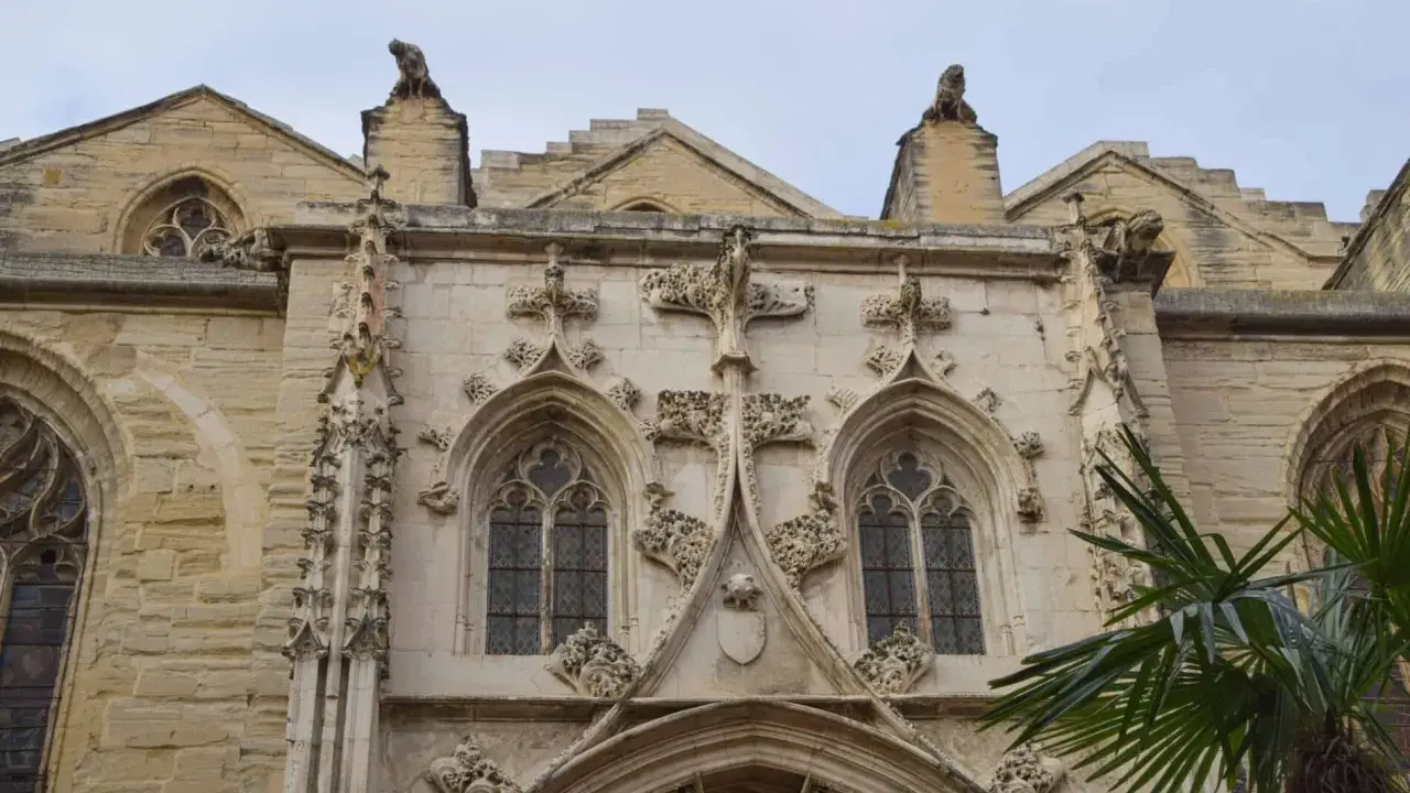 Détail architectural d'une cathédrale, un joyau du tourisme à Carpentras. Gargouilles et fenêtres gothiques sous un ciel couvert.
