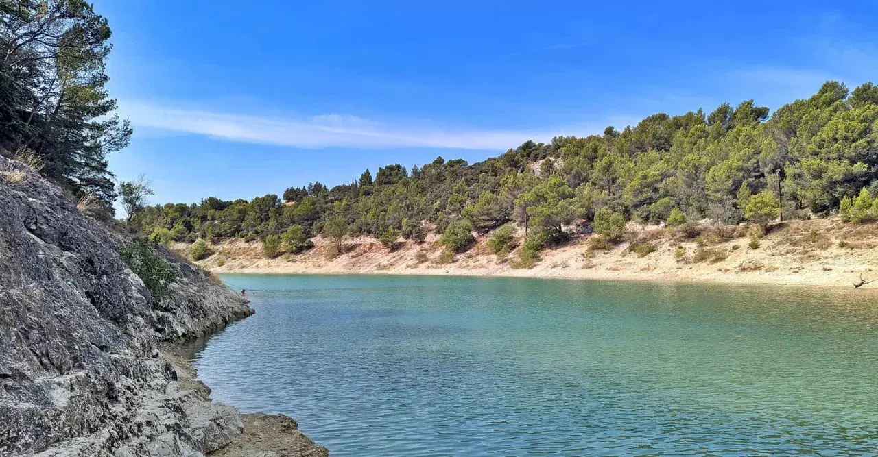 Le lac du Paty, aux eaux turquoise, est bordé de rochers et de collines verdoyantes sous un ciel bleu.