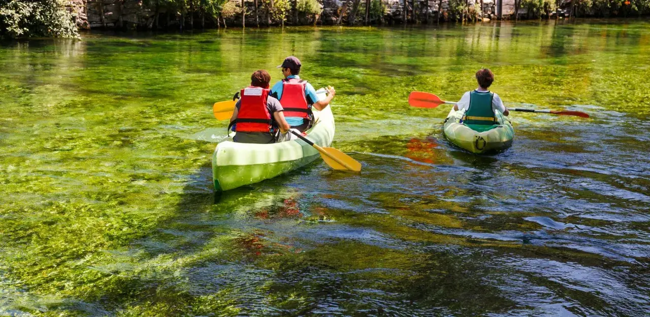 Trois personnes en canoë sur la Sorgue, profitant d'une balade paisible à L'Isle-sur-la-Sorgue. L'eau cristalline révèle la végétation sous-marine.