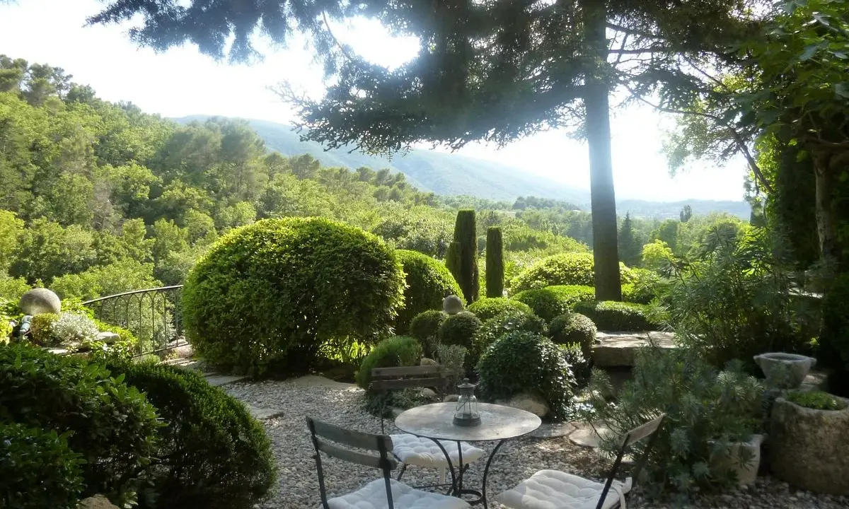 Le jardin de la louve, un havre de paix verdoyant avec une table et des chaises invitant à la détente, surplombe une vallée luxuriante.