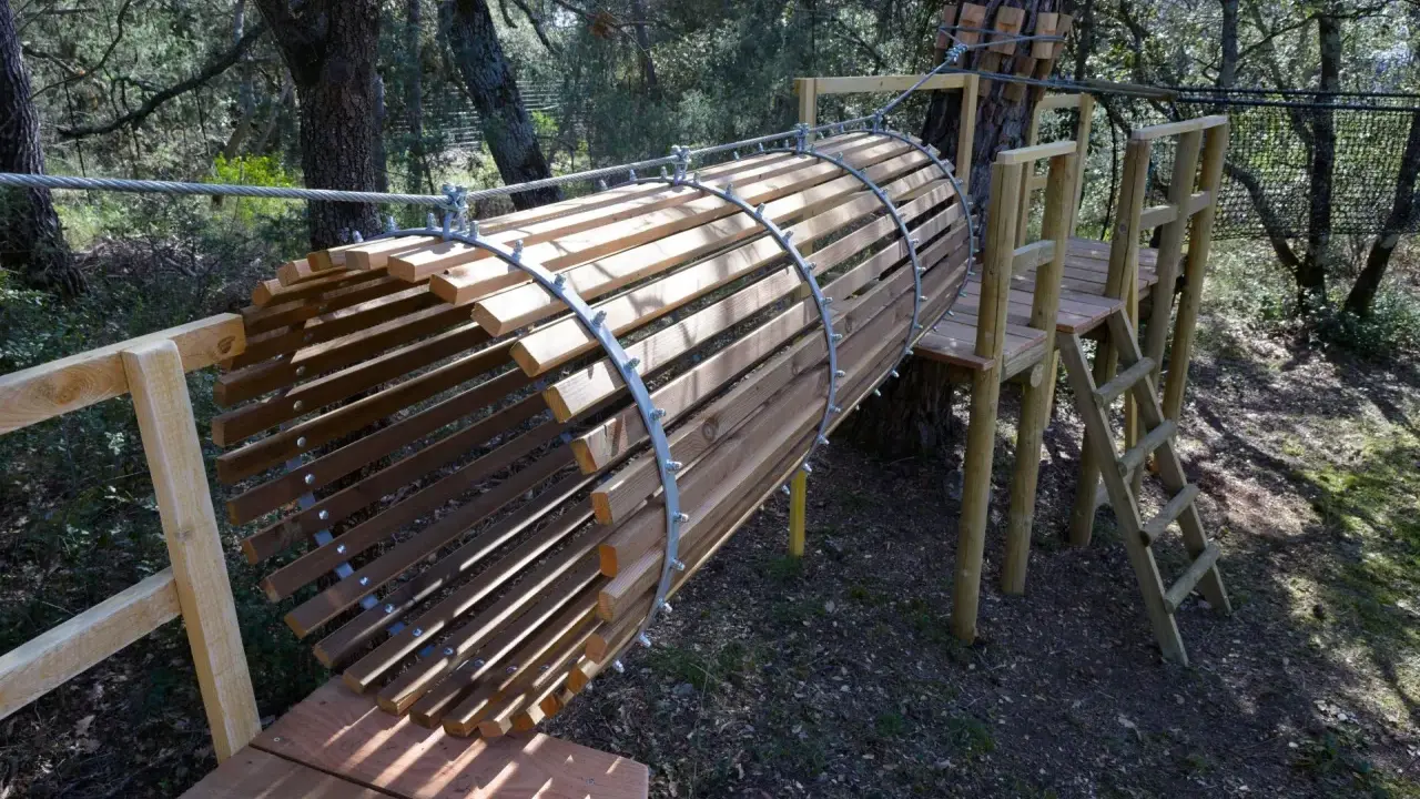Un tunnel en bois et métal, partie d'un parcours aventure dans la forêt enchantée Venasque. Une échelle mène à une plateforme.