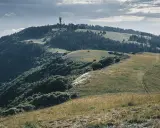 Vue panoramique du Moure Negre, avec une tour de télécommunication au sommet, des collines verdoyantes et un sentier sinueux.