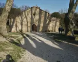 L'église de Vaugines, baignée de soleil, accueille deux visiteurs. Les ombres des arbres dansent sur sa façade de pierre.