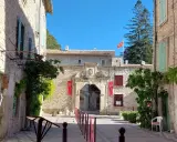 L'entrée majestueuse du **château de Thézan** s'ouvre sur une cour pavée, ornée de drapeaux rouges et d'une végétation luxuriante.