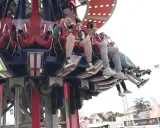 Des jeunes s'amusent dans une attraction de la fete foraine 84, leurs pieds balançant dans le vide.
