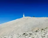 Le Mont Ventoux, sommet aride sous un ciel bleu intense, dominé par une tour de télécommunication.