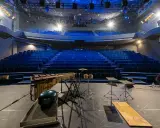 Scène de concert vide avec sièges bleus, marimba, batterie et projecteur, prête pour un spectacle à la Scala Provence.