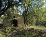 Ancienne bâtisse en pierre avec une arche, entourée d'arbres feuillus et d'une clôture en bois. Un lieu paisible dans le parc de l'arbousière.