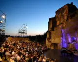 Public venu pour le festival de Gordes, une foule assise attend un concert au crépuscule, avec un piano sur scène et des structures métalliques.