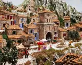 Une **crèche provençale** animée avec des santons, des maisons en pierre, un âne, un chariot et une fontaine, le tout dans un paysage rocheux.